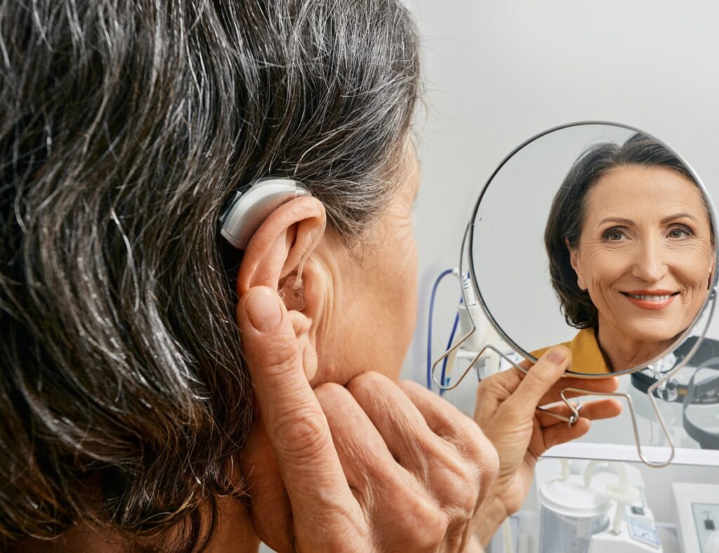 woman smiling in reflection at herself pointing at hearing aid